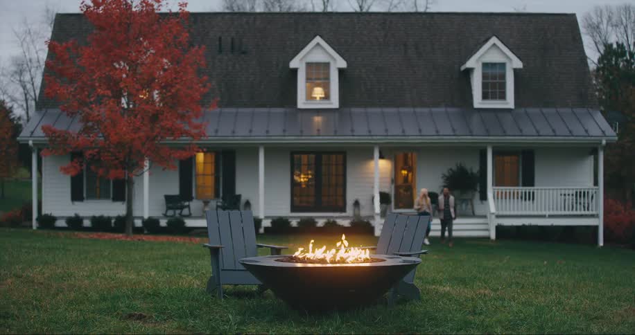A couple walks out of a house towards a fire pit