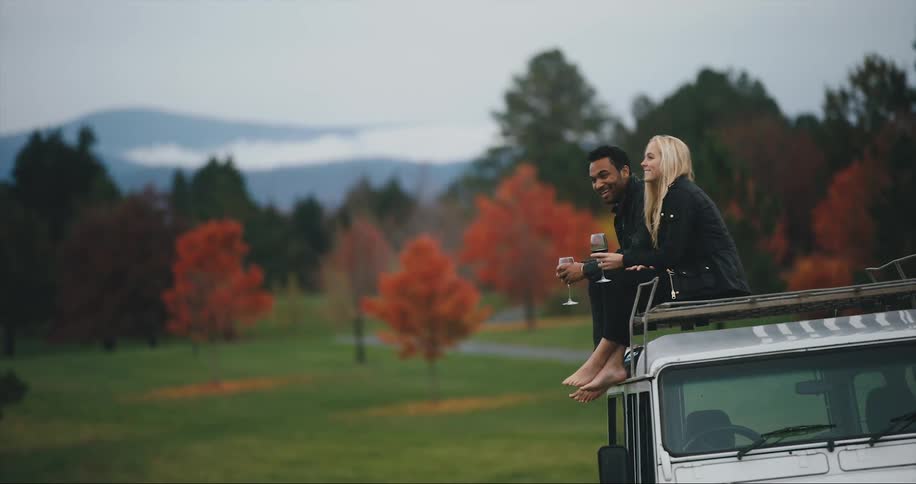 Couple sits on the roof of a vehicle and drink wine in the fall