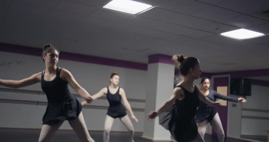 Four ballerinas dance in a studio that has a large mirror on a wall