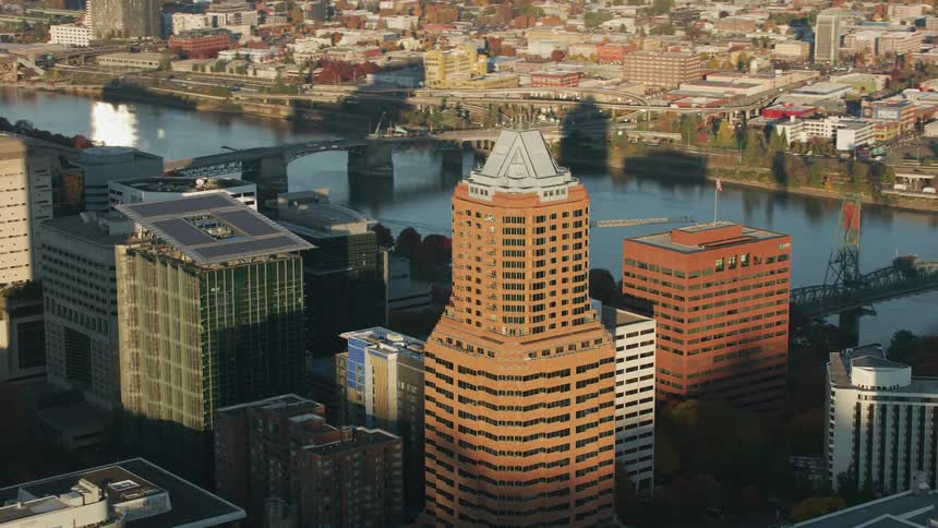 The sun shines on tall buildings and skyscrapers downtown along the river as traffic moves on the highway