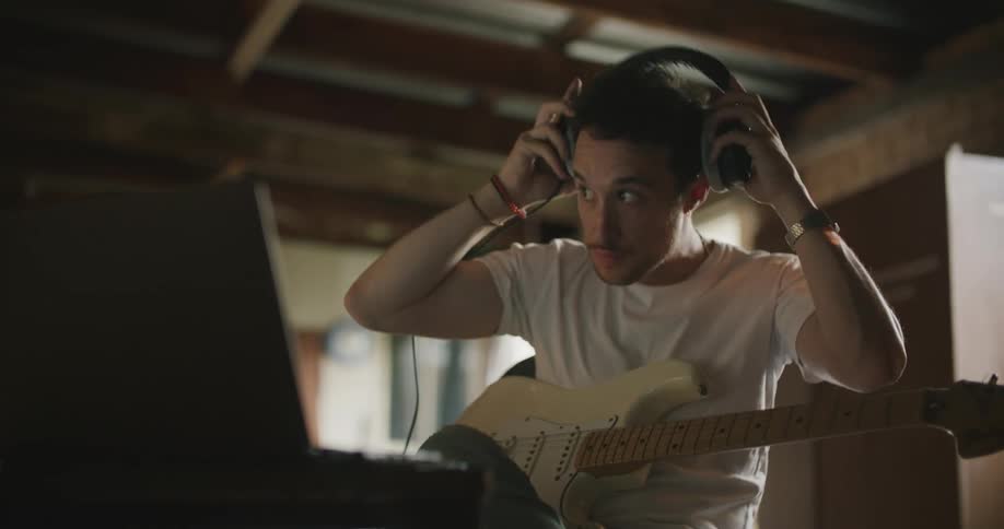A man is playing guitar indoors and wearing headphones