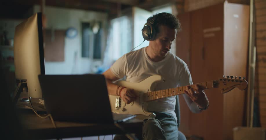 A man is playing guitar and wearing headphones
