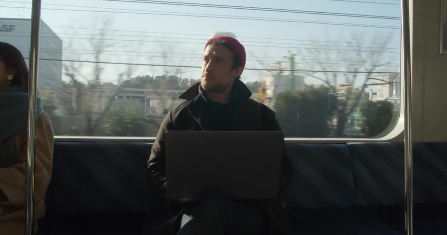 Man sits on public transportation working on apple laptop