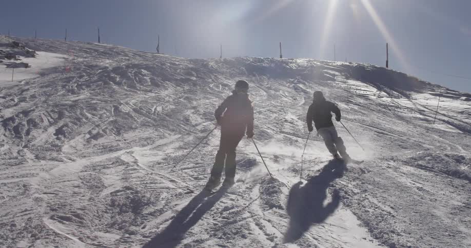 Two people ski together down a slope