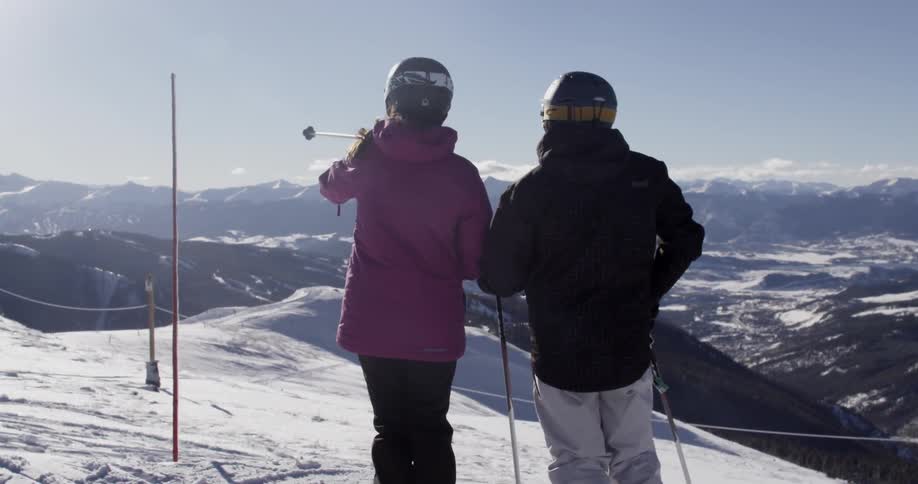 Two people stand on a ski slope on a sunny day