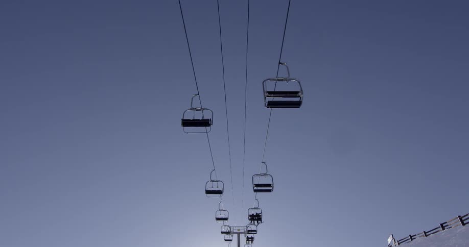 A ski lift transports some people across on a sunny day
