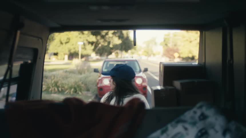 Two women load cardboard boxes and bags into the back of a van in a parking lot