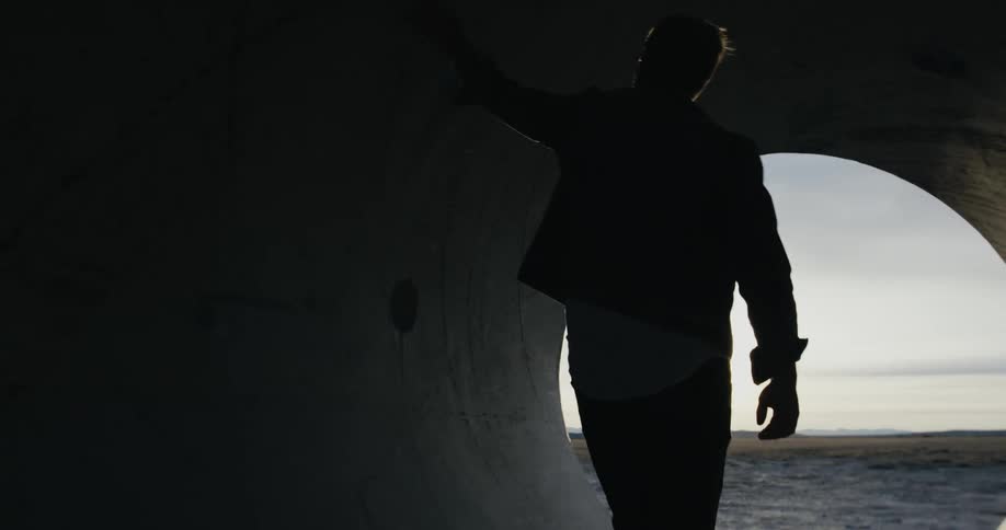 A man walks in a large sewer pipe sitting outside in an open area