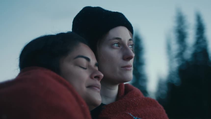 Two women sharing a blanket cuddled together looking sentimental and emotional