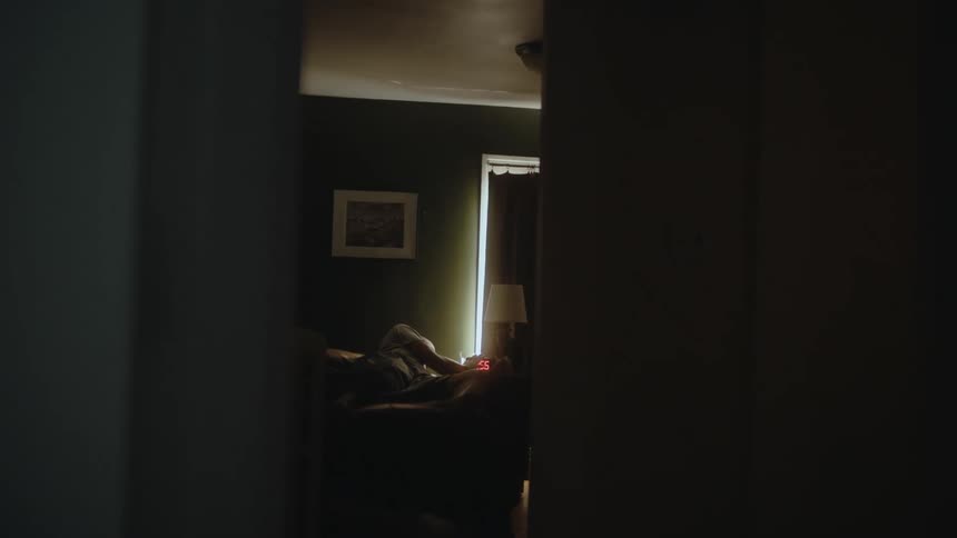 A man reaches over to turn off the alarm then sits up in bed still half asleep