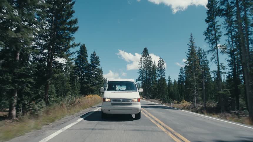 Suv passes white van as both vehicles drive along road through forest
