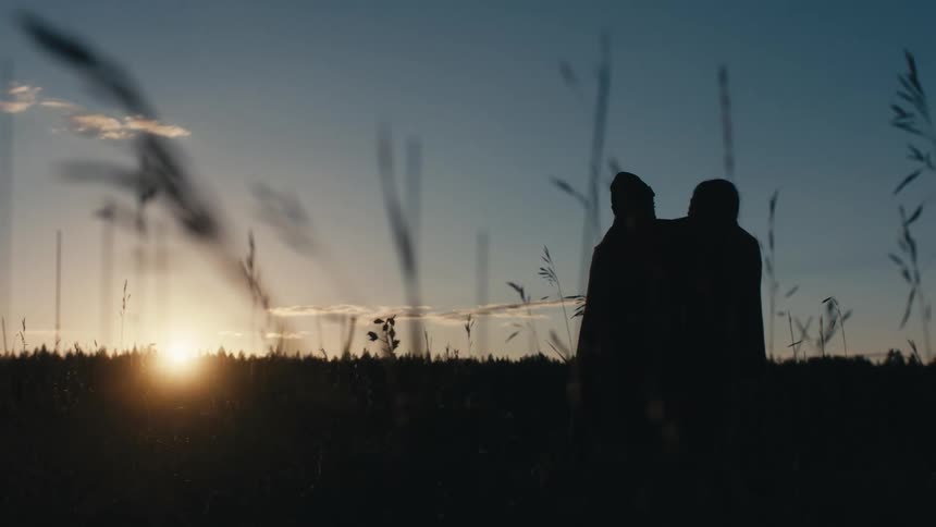 Two women wrapped up in the same blanket standing in a field watching the sun rise