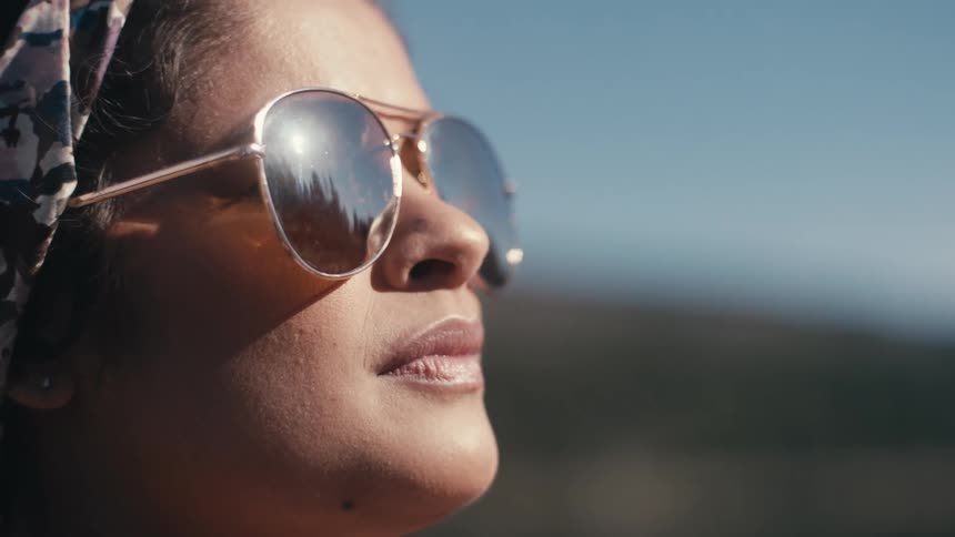 The sun shines on the face of a woman outside wearing sunglasses