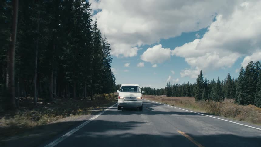 A white van travels on an empty rural highway on a bright sunny day