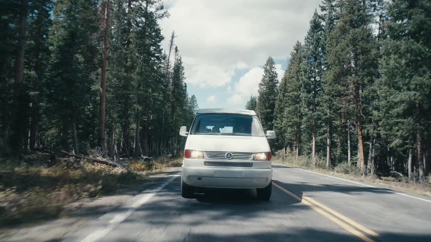 A van travels along a road through a woodland during the day