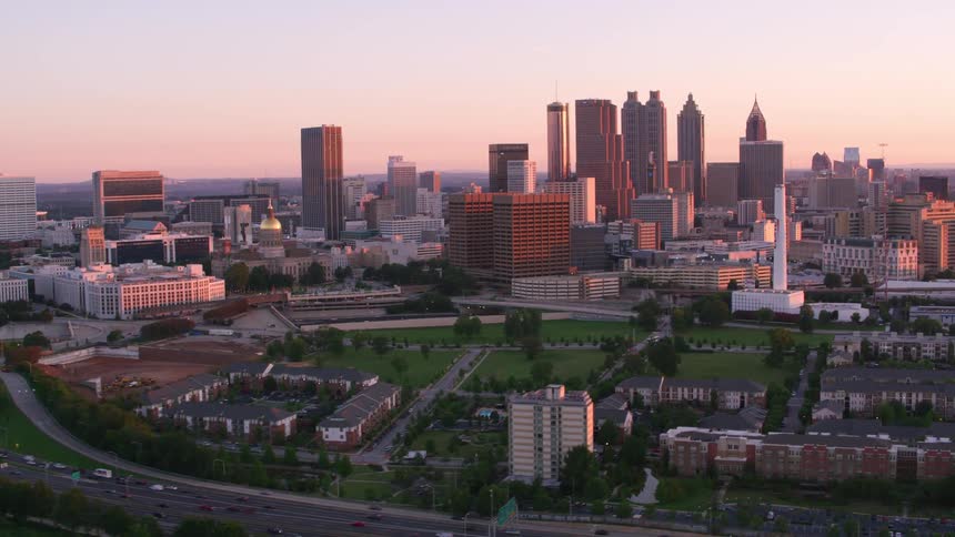 The sun shines on tall city buildings and skyscrapers as traffic moves on the streets