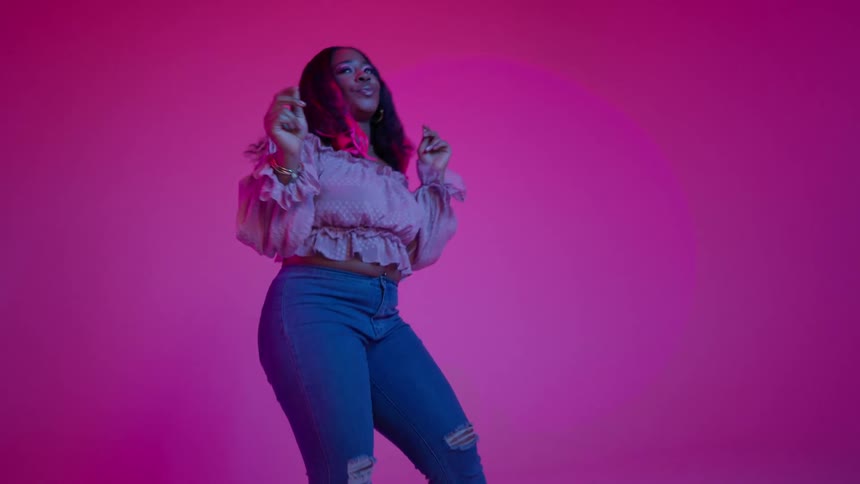A woman with pink streaks in her hair dances and poses in front of a pink background