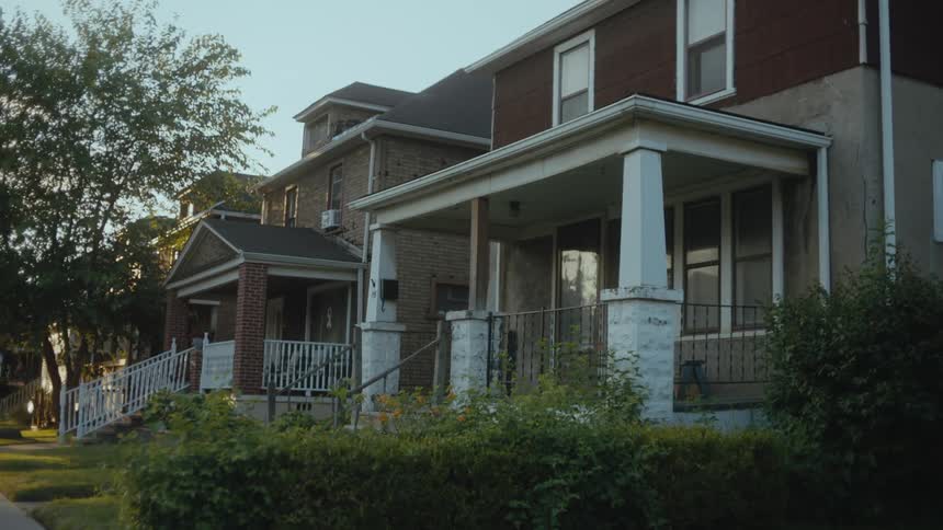 Bushes in front of a house in a neighborhood move in the breeze under a clear sky