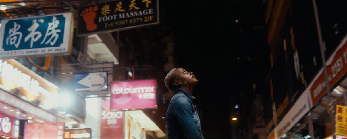 Woman stands in street at night near store fronts looking up at building