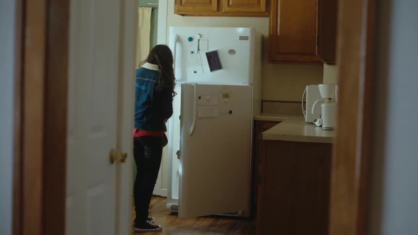 A girl walks over to the fridge then a corkboard