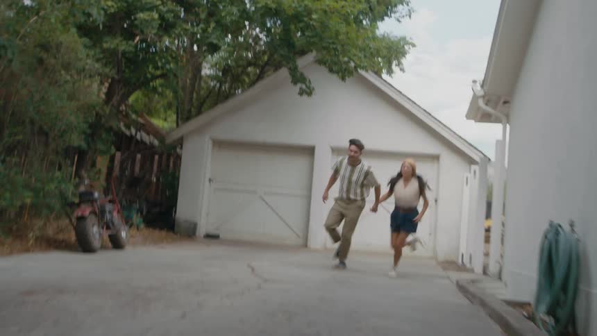 A couple runs down their driveway holding hands