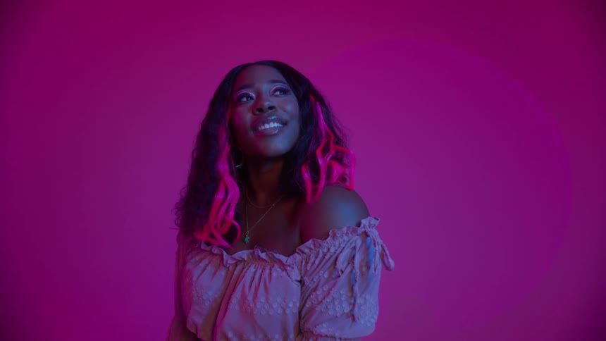 A black woman is smiling and posing with a hot pink wall behind her