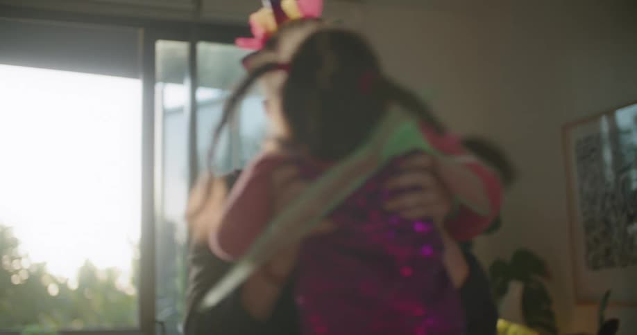 A dad picks up his little girl and twirls her around the living room