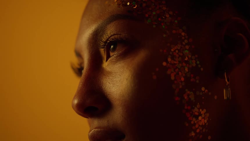 A teenage girl with sparkles on her face opens her eyes and looks ahead
