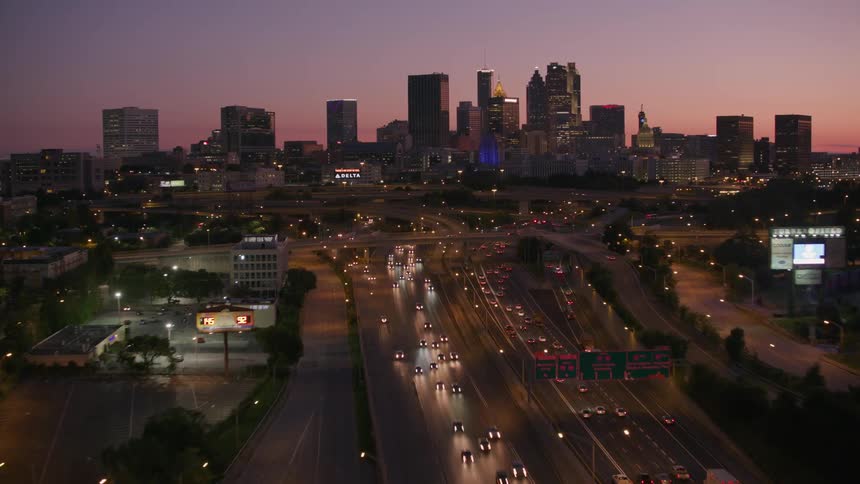 Tall buildings and skyscrapers stand out against a pink sky as heavy traffic on the freeways moves in and out of the city