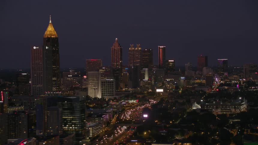 Heavy traffic flows down divided controlled access highway running through middle of the city at night