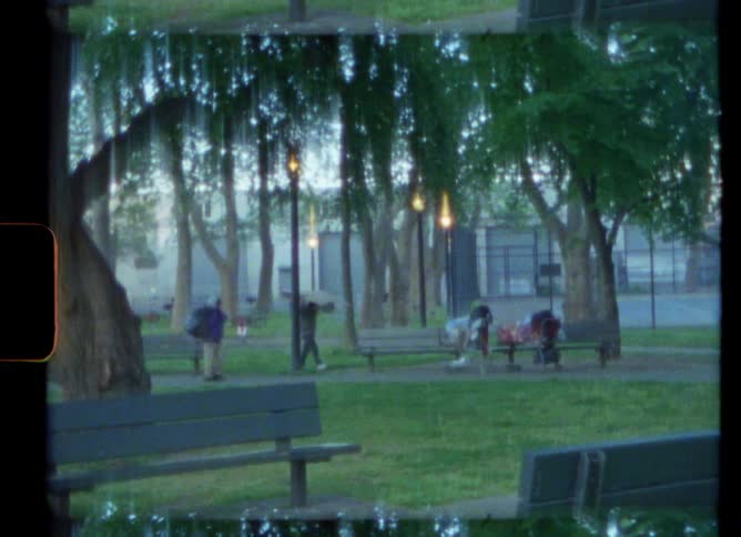 People carry things walking past two people on benches in the park