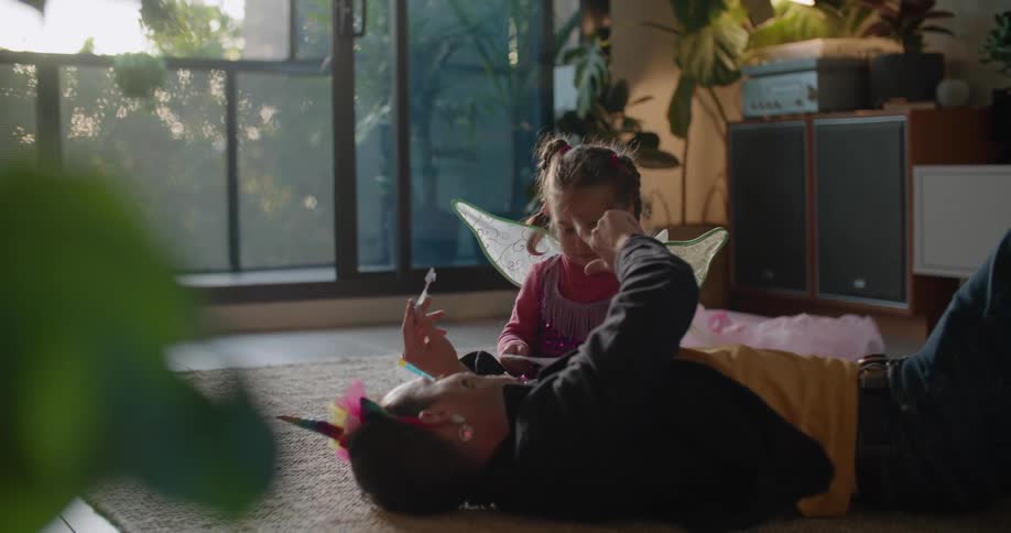 Father and toddler daughter wearing costumes playing over the rug on the living room at morning