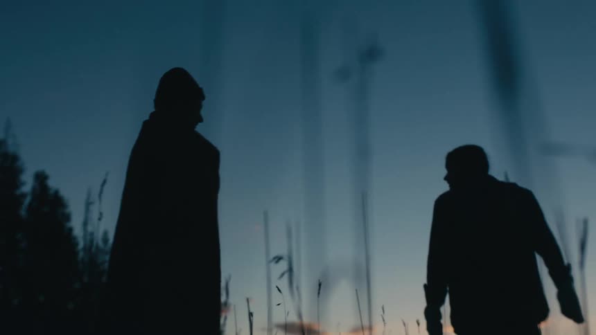 People silhouetted against the sky walk across field to face red horizon
