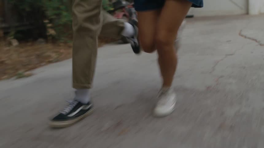 A boy and girl run through a neighborhood holding hands