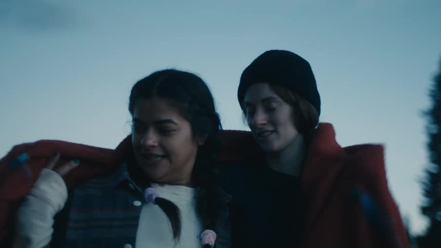 Two women standing in clearing near forest and looking around share throw