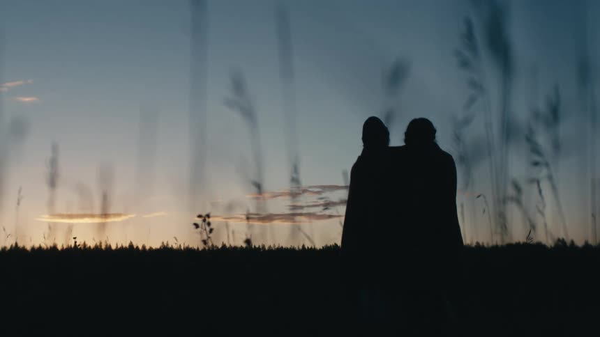 Silhouette of a young couple hugging on a tall grass field at sunset