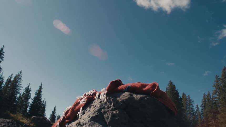 A woman sitting on a blanket atop a boulder turns her head and smiles before rising to her feet