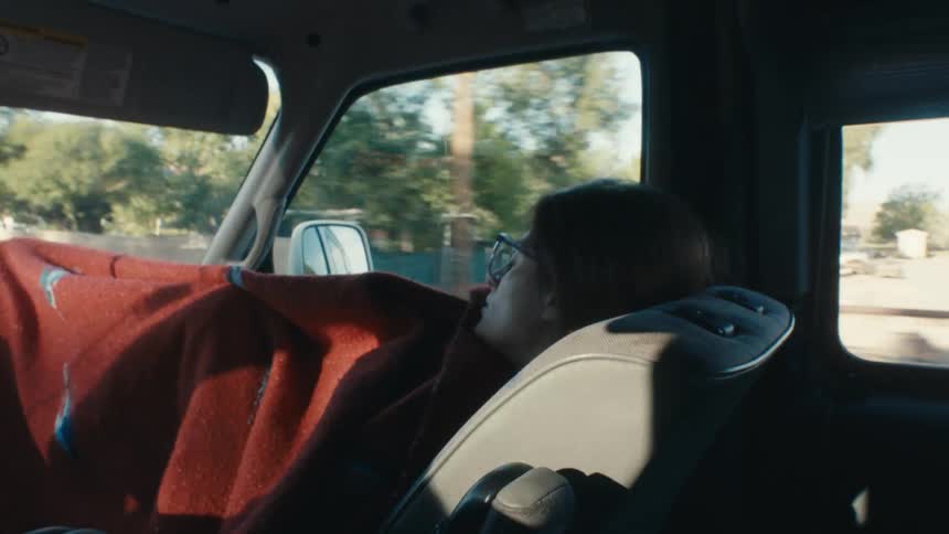 A woman is sleeping in the passenger side of an automobile traveling on a road