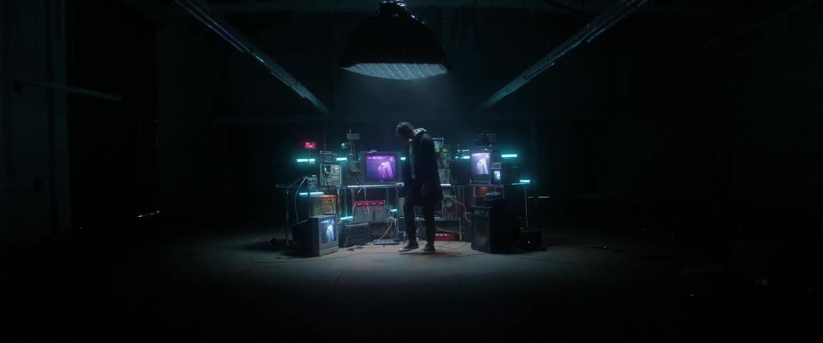 A man walks into a room with old televisions and monitors and sees himself on all the screens