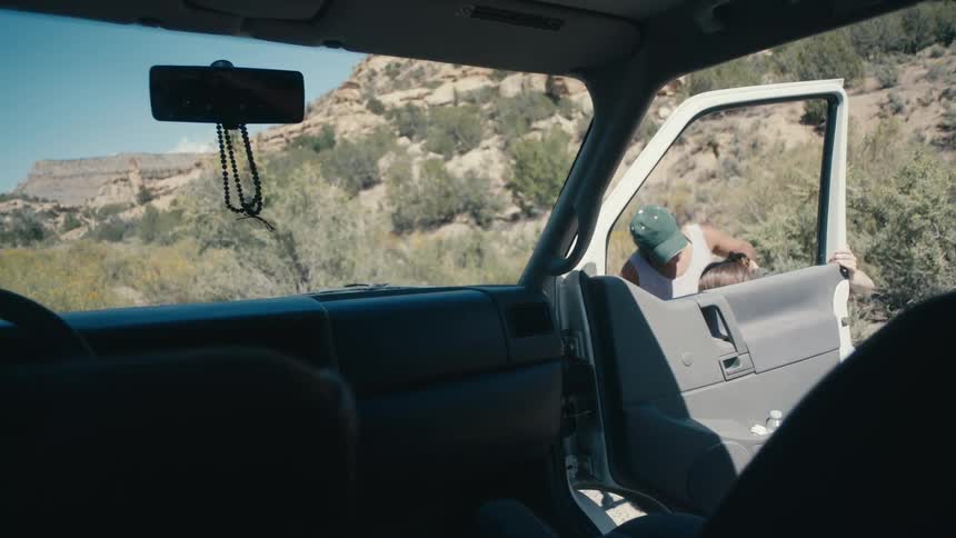 A teenage girl gets out of a truck parked at the side of a road by a cliff and throws up as her mother runs around the truck to help and comfort her