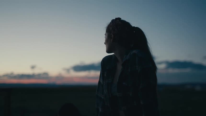 A woman sits outdoors in a vast countryside at sunset