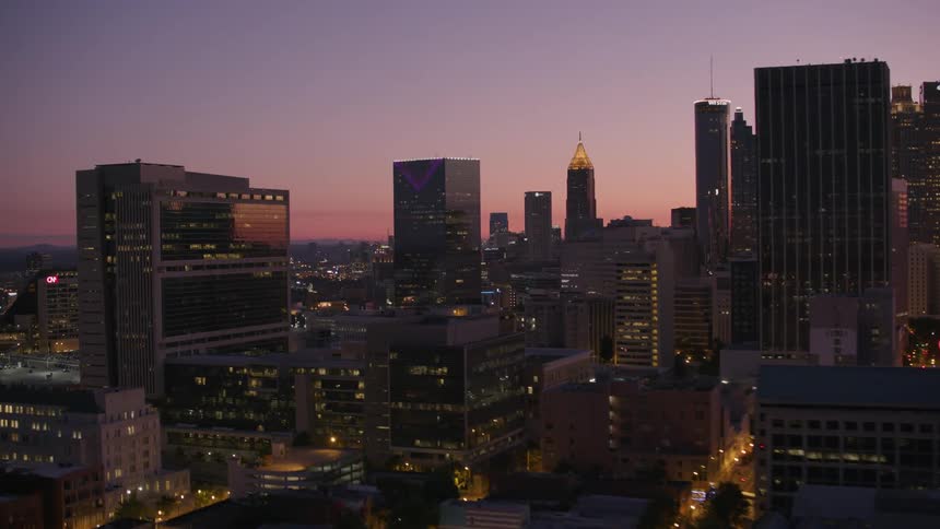 Lights on downtown skyscrapers and buildings glow as the pink sky grows darker
