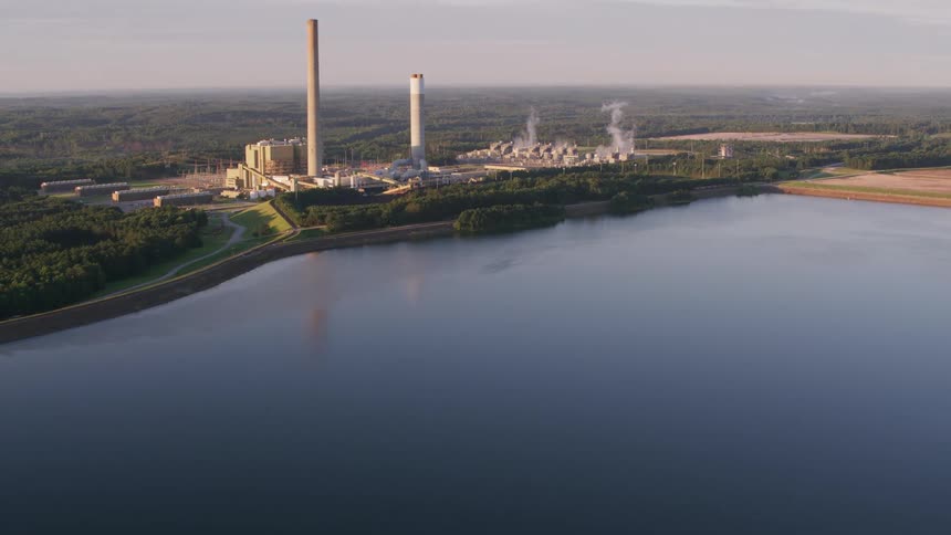 Tall smokestacks from a factory along the coast reach high the sky as smoke rises from smaller chimneys
