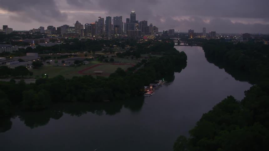 Aerial view of cars moving on a bridge over a river near the city skyline on an overcast day at evening