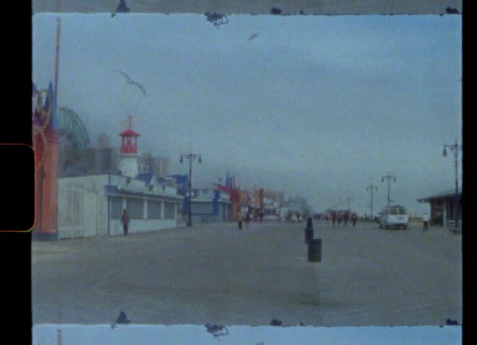Birds fly overhead as pedestrians walk past stores and nearby ferris wheel