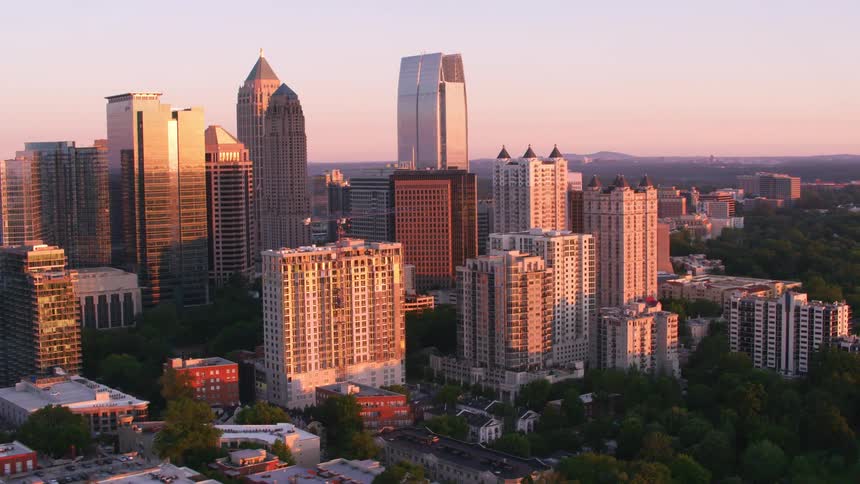 The sun shines brightly on tall city buildings and skyscrapers downtown surrounded by trees
