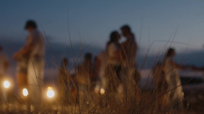 Couples surrounded by car headlights dancing on a rural field at sunset