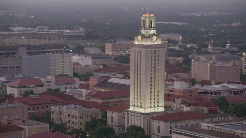 A clock tower looms over the surrounding buildings in a city in the evening