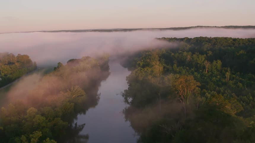 An aerial view of fog covering a river next to a forest
