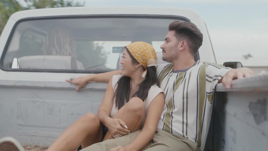 Couple sits in back of truck driving through neighborhood with large houses